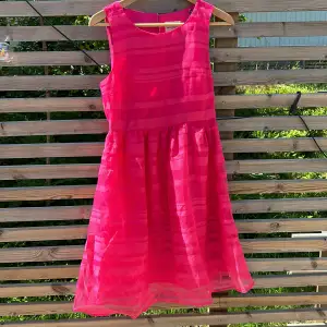 Rosa klänning med utställd kjol från Holly & Whyte/Lindex i stl 36. Stängs med mässingsfärgad knapp i nacke, och har en dold dragkedja på vänster sida.   Perfekt sommarfestklänning!   Aldrig använd, lapparna kvar. 