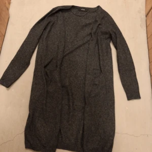 Lång kofta - Grå mörk melerad Använd i bra skick Osäker men kan vara wool blend  Har 2 fickor