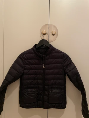 Moncler 10-12 år - Tunn dunjacka Moncler (äkta) stl 12 år. Skulle säga att den passar från 8 års ålder upp till 11/12 år (beroende på barnet såklart). Namn o telefoner skrivet på insidan som jag strök över i denna annons. Bra skick! 