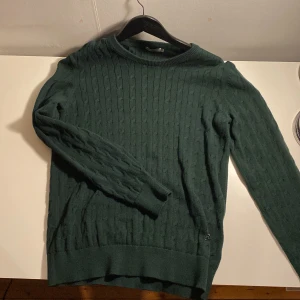 J.Lindeberg Mörkgrön Tjocktröja L - En mörkgrön, stickad tjocktröja från J.Lindeberg med hög kvalitet som är väldigt snygg och skön att ha på sig. I mycket bra skick. Nypris 879 kr.