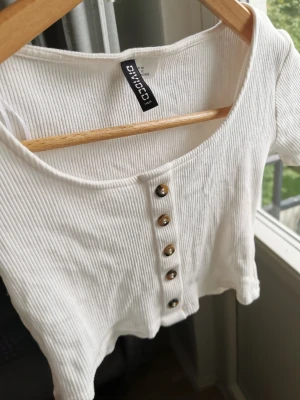 H&M croptop - Vit croptop med knappar. Bredd 32 cm, längd 29 cm. Finns djur i hemmet så kan förekomma katthår. 