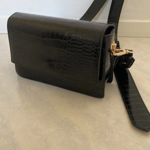 Svart väska - Säljer min oanvända väska med ett jätte fint tjockt band i skinnmaterial och gulddetaljer.