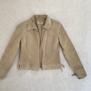 Beige mockajacka - Tunnare jacka i mocka med snörningar på ärmarna och sidorna, från märket Joy! 🤎