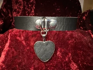 Kärlekscollar Collar m läderhjärta bdsm fetisch fetish rave Pride party fest statement Rock Metal Goth Punk  - Romantisk choker med svart hängande ”läderhjärta”.  Justerbar med tryckknappar därbak.Band av konstläder som är 2,8 cm brett med tryckknappar, hänget med läderhjärtat är 3,5 cm långt. Längd på chokern varieras med tryckknappar mellan 33 & 40cm.