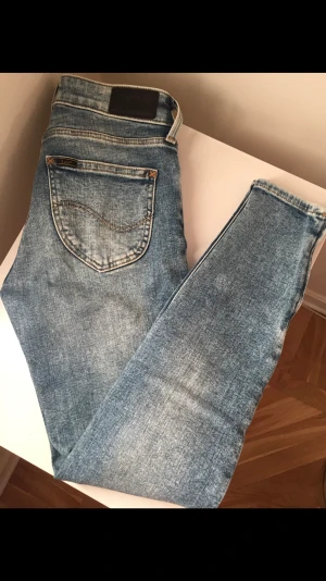 Snygga Lee jeans - Använda 2 gånger, nyskick. Lite mer blå än på bilderna. Smal passform med smala lår och avsmalnande benslut i ankellängd med dragkedja på utsida benslut.  