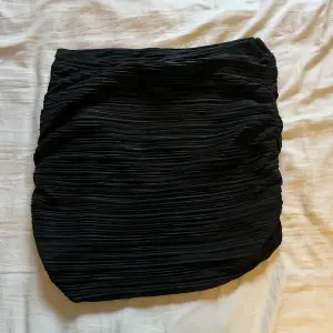 En väldigt fin, svart kjol som har resår på ens sidan vilket gör att den åker upp lite där. Sitter bekvämt och är i bra skick.
