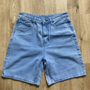 Blå jeansshorts - Oanvända ljusblå jeansshorts utan stretch. Framfickorna är äkta. 85% bomull 15% polyester. Säljs då de är för små för mig. Mått mätt platt: midja 35cm, längd 47cm och innerbenslängd 20cm