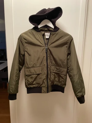 Pilotjacka - Olivgrön och svart jacka med luva och 2 st fickor i mycket fint skick.