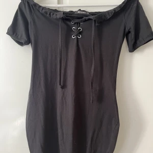 Off shoulder klänning - En svart off shoulder klänning med knytning fram vid bröstet. Den är figursydd så den sitter verkligen jättefint på kroppen. 