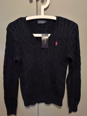 NY! Polo Ralph Lauren V-ringad tröja - Oanvänd marinblå kabelstickad tröja från Polo Ralph Lauren i storlek M. 