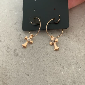Guldiga kors örhängen - Ett par jätte snygga guldiga kors örhängen med en silver diamant i mitten🫶🏻. Ordinarie priset för dessa örhängen är 29kr men säljer pågrund av att jag aldrig har användt dom. (Helt nya)