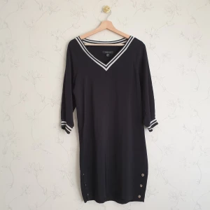 Svart sportig tunika - ☀️FÖRST TILL KVARN!☀️ En svart lång topp eller tunika med randiga  stretchiga svartvita revärer som mudd och halsringning. Tre silvriga tryckknappar på vardera sida av tunikan som kan öppnas. Det är trekvartsärm som längd på ärmarna. Från New Yorker.