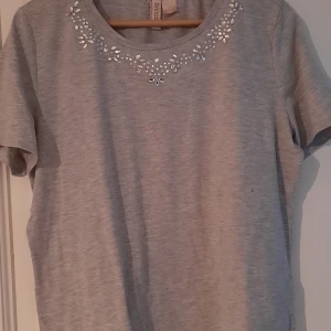 T- shir - Superfin ljusgrå t-shirt med "paljetter" från hm. Storlek L.   Säljes då den inte kommer till användning. Hör gärna av dig vid frågor eller funderingar. 