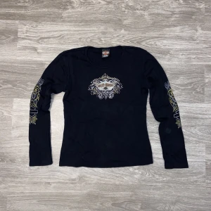 Harley Davidsson långärmad  - En Harley Davidsson långärmad tröja, dam modell. Flesta stenar sitter kvar men någon enstaka som ramlat, märks ej av. Mått: längd ca 57.5cm. Armhåla till armhåla ca 46-47cm. 