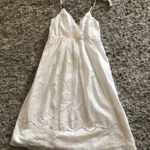 Vit kort klänning från Lindex  - Vacker vit kort sommarklänning från Lindex. Strl 36. Broderier nertill och pärlor uppe på banden. Reglerbara band.
