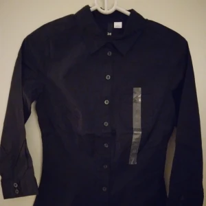 Svart skjorta / blus för kvinnor. Bomull. Strlk: 34 / XS. HELT NY & OANVÄND.  - Svart skjorta / blus för kvinnor. Bomull. Strlk: 34 / XS. HELT NY & OANVÄND. Felfri. Tags sitter kvar sedan inköpet. Säljer även en likadan fast vit i samma storlek, den vita är dock lite använd.
