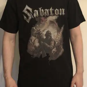Detta är en cool svart T shirt med Sabaton tryck. Den är i hyfsat skick men trycket är något slitet. Denna T shirt är i storlek i Stl L.