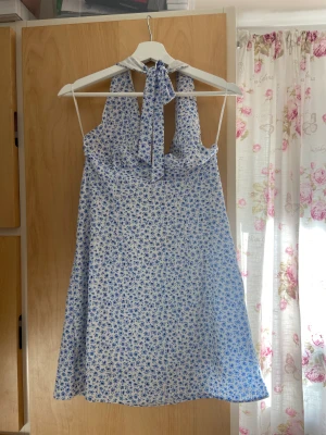 Blåblommig klänning  - Otroligt söt klänning, med blåa blommor. Kort och man knyter den i nacken, har även en dragkedja på sidan. Använd fåtal gånger och väldigt fint skick