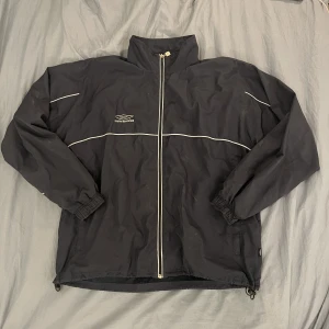 Umbro vindjacka - Köpt på second hand, använts ett fåtal gånger av mig. Säljer då den är lite stor för mig. Jackan har lite lerfläckar men är nästan helt säker på att de går bort i tvätten. Kan även skicka fler bilder vid behov☺️