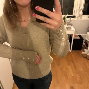 V-ringad stickad tröja - Säljer denna v-ringade stickade tröja med pärlor på armarna då den inte längre kommer till användning. Den är super mjuk och har en jättefin beige färg💖