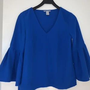 Blå v-ringad blus - Kornblå blus i polyester från HM i stl 34. Trumpetärm. Bra skick.