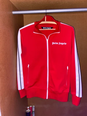 Palm Angels kofta  - Röd Palm Angels kofta i storlek S,  Palm angels koftan är såklart äkta har alla bevis för att kunna visa att den är äkta med taggarna och sånt, koftan är i väldigt väll bevara skick, koftan är felfri från hål och annat. Ny pris när jag köpte var 3499kr