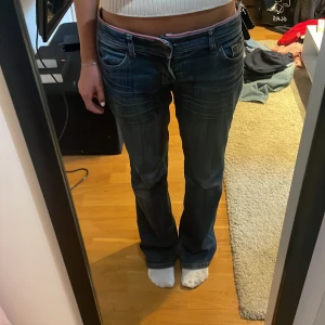 Lågmidjade jeans  - Blå lågmidjade jeans med rosa kant. Säljer pga för stora för mig. Är vanligtvis storlek 25. Skulle säga att de passar folk med storlek 27 också. Lite slitna längst ut i benen. Pris kan diskuteras