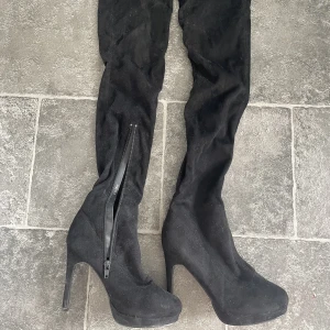 Lårhöga stövlar - Lårhöga stövlar stl 37 Använda en gång. Så fint skick. Dra på stövel med blixtlås vid smalbenet. Reflektion av ljuset så de ser ut att skifta i färg. Men de är helsvarta.