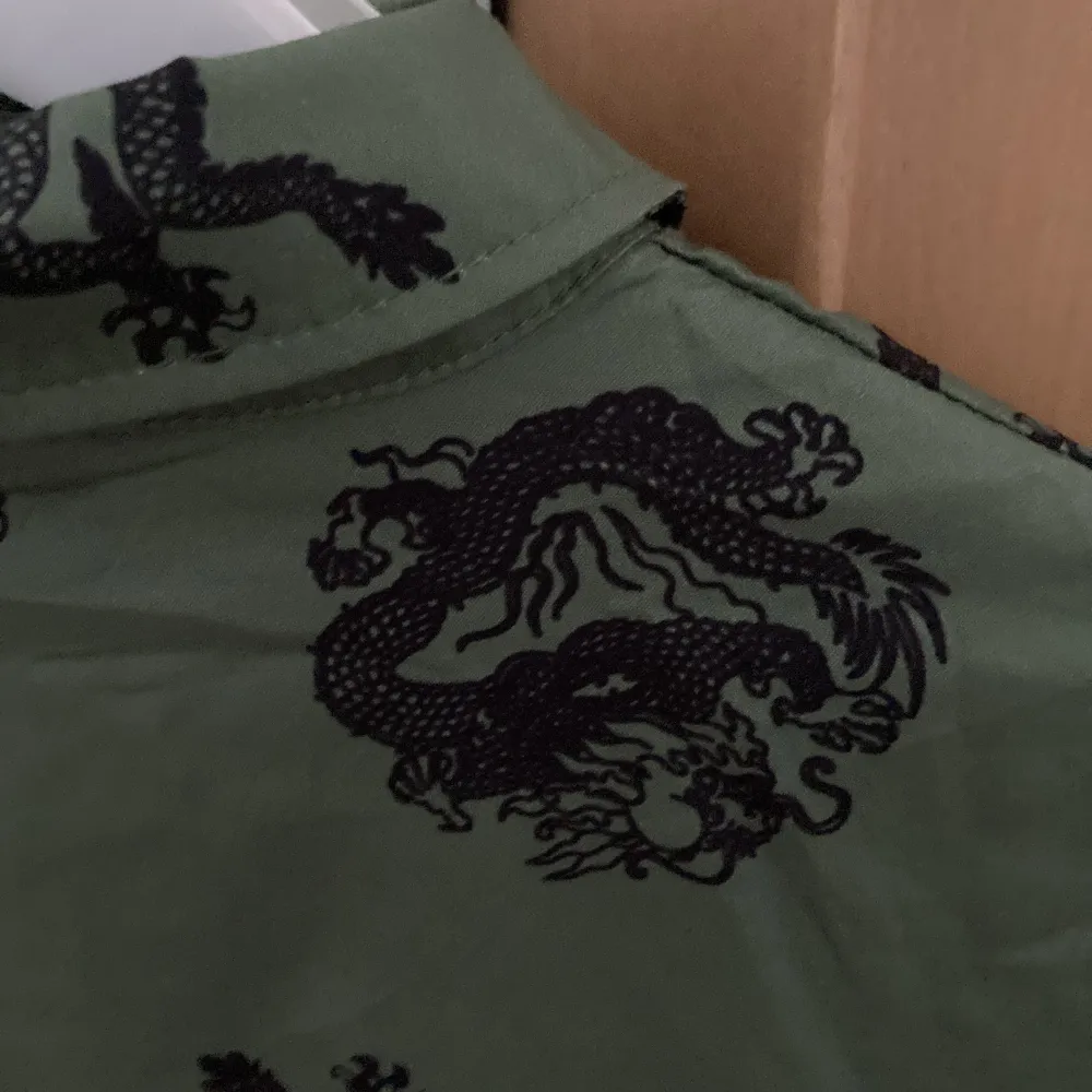 En jättefin grön skjorta med svarta drakar på. Den sitter som en oversized M eller som strl L. Frakt ingår ej . Skjortor.