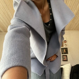 Ljusblå sommarkappa - Supersöt ljusblå (mer blå än grå som på bilden), tunn, kort ullkappa med knytband. Säljes då den inte kommer till användning. 