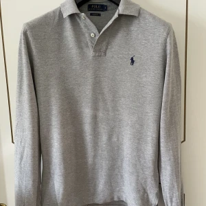 Ralph Lauren pikétröja  - Säljer en grå Ralph Lauren pikétröja i fint skick.   Tröjan gjord av 100% bomull  Nypris ligger på runt 1000kr