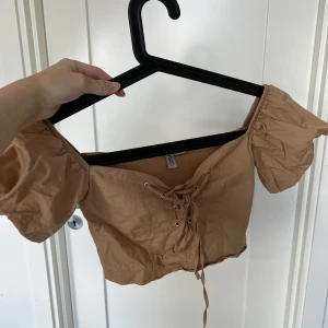 HM topp - Topp i mörk beige med knytning fram. Fint skick. Storlek xxs.