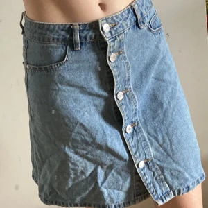 Jeansskjol - En välbehållen blå skjol med knappar fram.  Midwaist . Två fickor fram och bak.