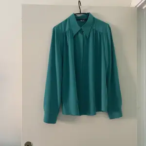 En grön/turkos blus i 100% polyester. Köptes på second hand men har sedan dess använts 1 gång. 