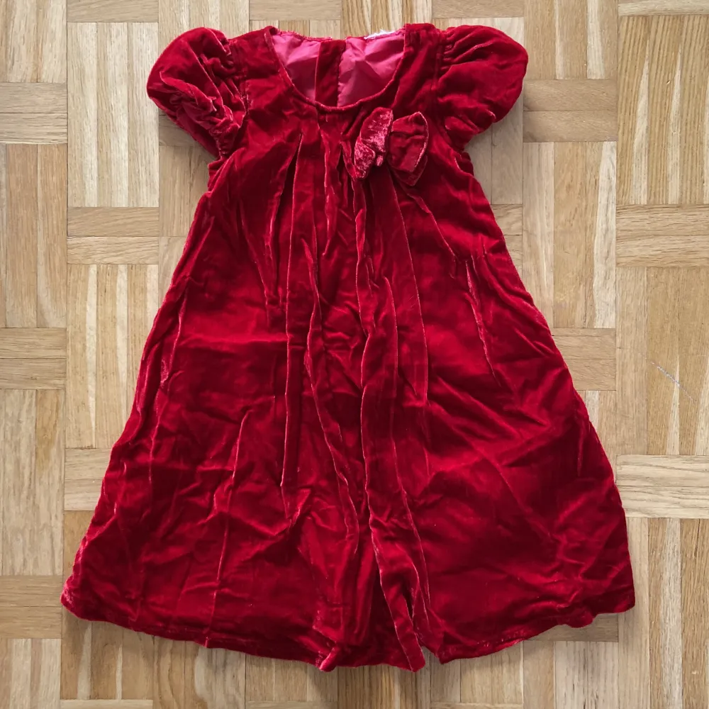 Röd klänning med en liten rosett, för barn. Jag hittar ingen storlek men hade själv på mig den som 4 åring, funkar säkert på 3-5 år.. Klänningar.