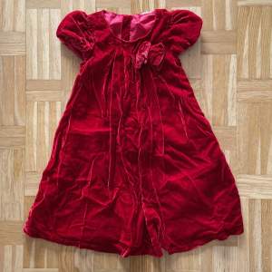 Röd klänning med en liten rosett, för barn. Jag hittar ingen storlek men hade själv på mig den som 4 åring, funkar säkert på 3-5 år.