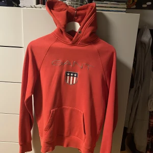 Röd Gant shield hoodie - Tja säljer min röda gant hoodie, den e knappt använd senast va runt 3 år sedan. Enda nackdelen är att de vita snören saknas men annars ingen skada, hör av er vid minsta lilla (orginal pris stax över 1000kr)