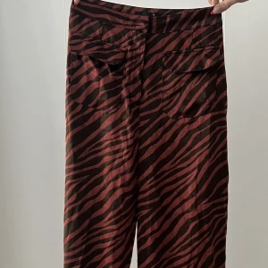 Plattade lösa byxor - low rise pants  - Mönstrade byxor i tunnt material, perfekt för våren och sommaren.  Färgen är röd/brun och svart. 
