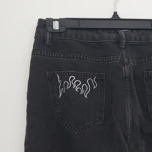 Jeans med broderade eldsflammor  - Båda bakfickorna har broderade eldsflammor, vida svarta jeans med hög midja.