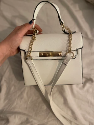 Vit väska med svarta kanter - vit Väska med långt axelband. Väskan har scarta kanter och guldiga ditaljer. Nästan aldrig använd. 