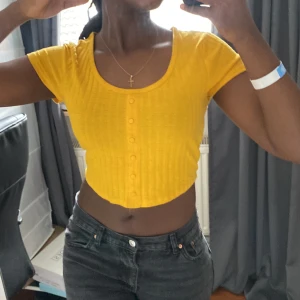 En gul croptop med knappar - *Knapparna går inte att knäppa, endast för style*  En fin gul topp som passar perfekt till sommaren. Använd ett fåtal gånger men finns inga synliga fel💛 Skriv för mer bilder!