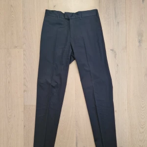 Byxor Filippa K - Marinblå Slim - Ett par marinblå och lätt blanka byxor från Filippa K med diskreta pressveck. Storlek 44. Slim passform. Knappt använda 