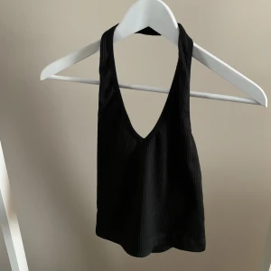 Halterneck topp - Svart halterneck topp i ribbat material med öppen rygg. Strl s. 60kr+frakt