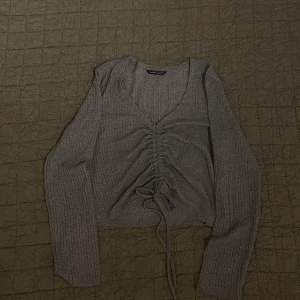 Ljusgrå topp med knytdetalj - En ljusgrå croppad topp med knytdesign som går att ställa in beroende på hur lång eller kort du vill att toppen ska vara. 