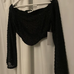 Svart topp - En svart glittrig topp med vida ärmar, i storlek M. Aldrig använd, bara testad. Prislapparna finns kvar. Helt ny!