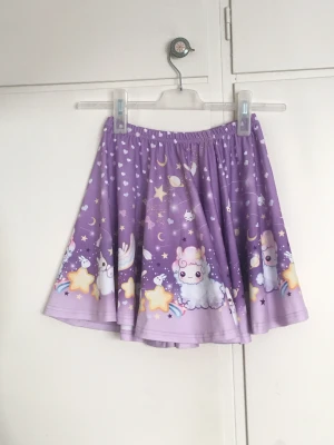 Lila kjol med mönster - Söt kjol från kawaii.se.  Syntetmaterial, sparsamt använd & i gott skick. Elastisk midja ca 60-80cm Kjolslängd ca 40cm. Pris inkluderar frakt.  Meddela vid frågor!