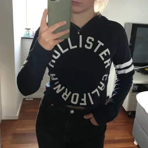 Långärmad tröja med luva - Mörkblå långärmad lite croppad tröja med luva från Hollister i storlek XS. Passar även mig som är S. Den har en fläck på ena armen, se bild 3. Den syns dock inte så mycket när man har tröjan på sig.