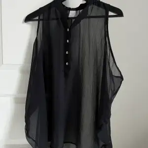 Transparent svart linne med knappar framtill. Breda axlar och lång i modellen. 