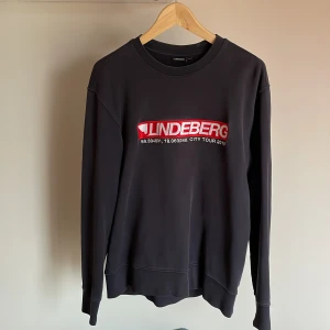 J.LINDEBERG SWEATSHIRT  - Strlk M, något mindre i storleken. Mörkblå kvalitativ tröja med broderade detaljer. Tröjan är något solblekt, ser därför lite mer vintage ut.
