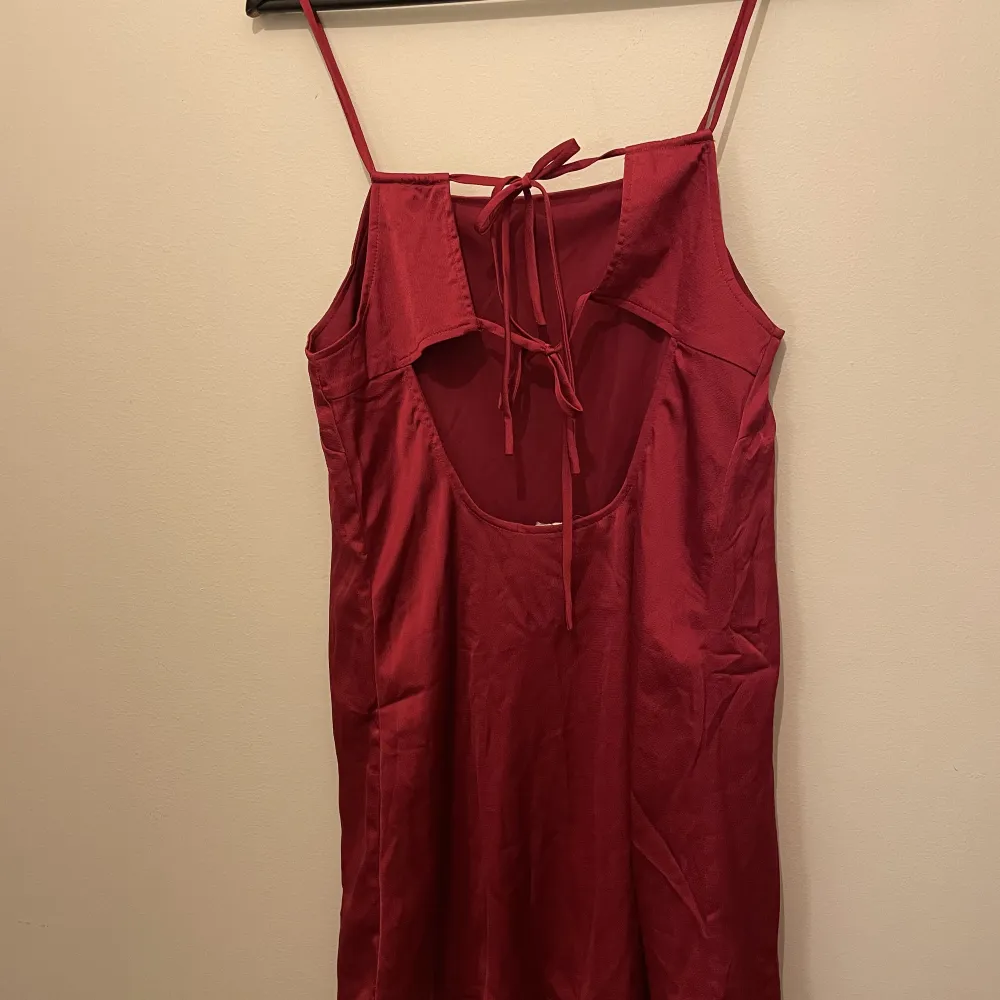 Röd klänning i silkigt material. Öppen rygg med fina knytband. Lite lös i modellen.  Minns ej var den är inköpt ifrån. . Klänningar.